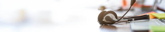 Ein Headset mit Mikrofon liegt auf einem Holzschreibtisch neben einem Laptop in einem hellen, sonnigen Büro. Symbolisiert Kunden-Support, Online-Beratung oder Servicebereitschaft.