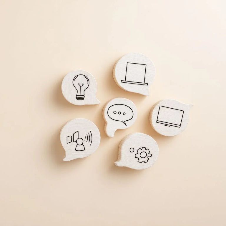 Sechs Holzmünzen in Sprechblasenform, die Symbole für Kommunikation, Ideen (Glühbirne), Technologie (Laptop, Bildschirm) und Struktur (Zahnrad) zeigen. Symbolisiert Konzepte und Strategie.